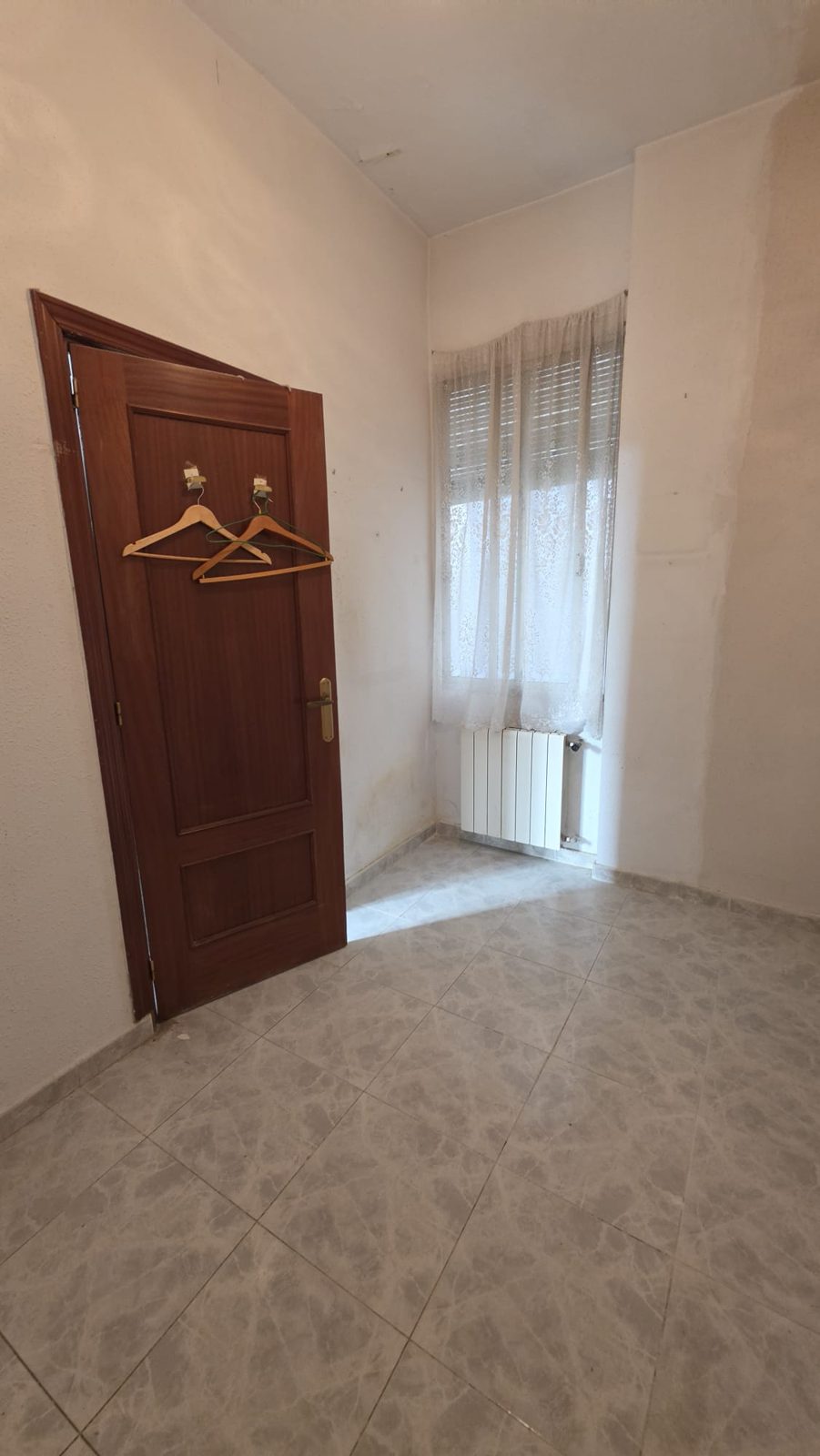 Segunda habitación con puerta de madera, ventana y radiador