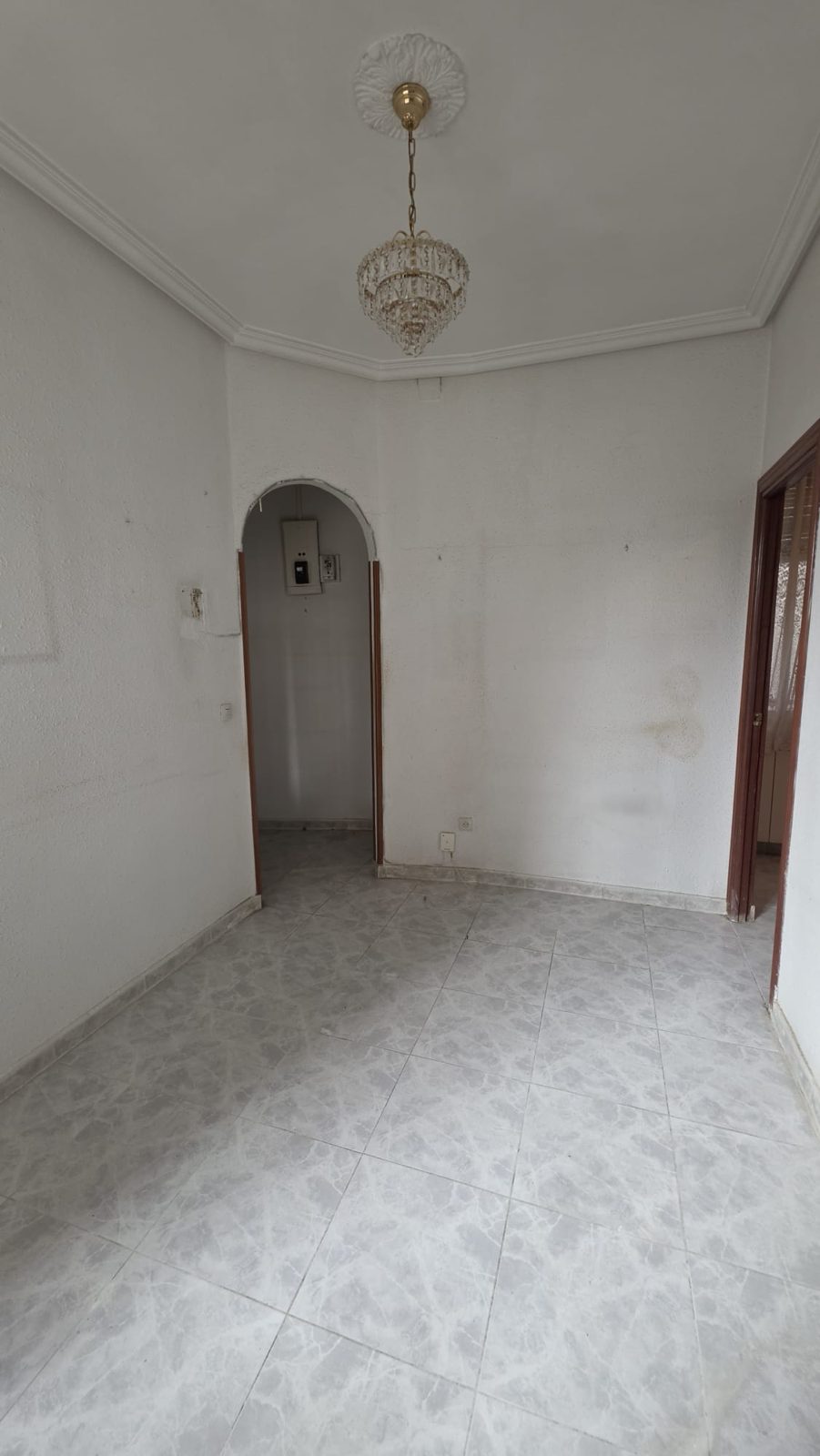 Salón de la vivienda con molduras de escayola, lámpara de cristal y arco de paso